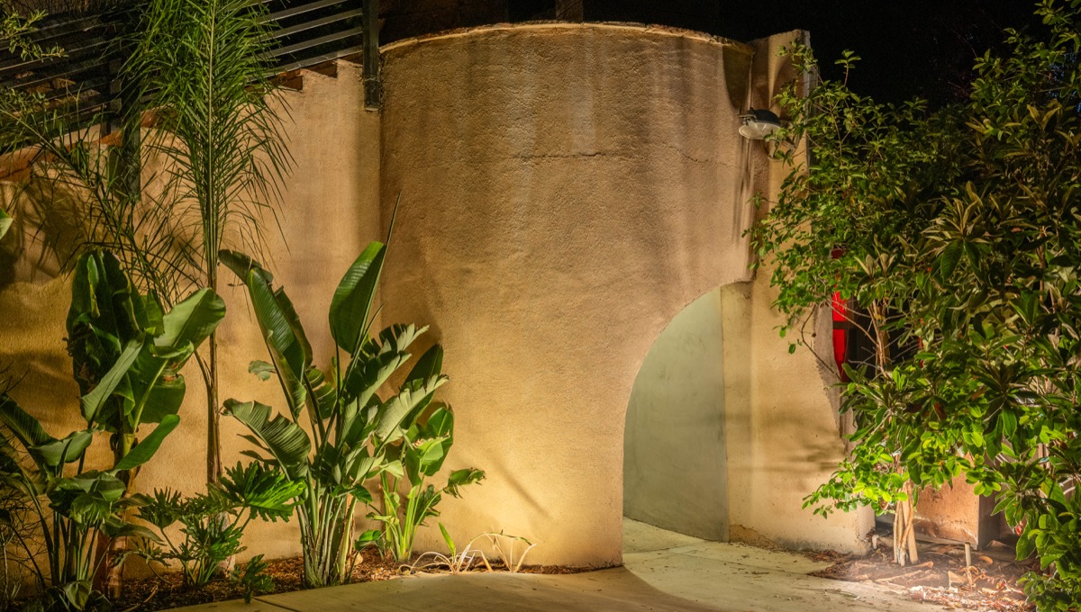 Adobe wall and tropical foliage lit at night on the estate grounds